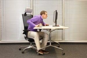 Mann som sitter med dårlig ergonomi foran PC